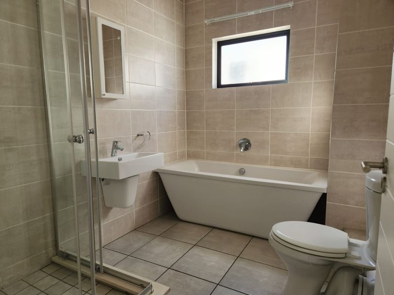 A clean, modern bathroom featuring a freestanding bathtub, a separate glass-enclosed shower, a wall-mounted basin, and neutral floor-to-ceiling tiling.