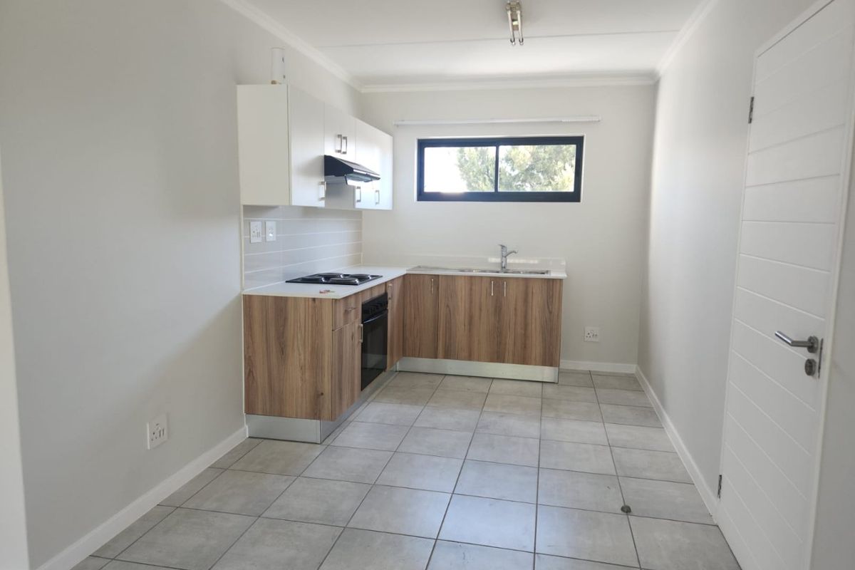 A clean, modern kitchen featuring wood-finish lower cabinetry, white upper cabinets, a built-in oven and hob, and neutral tiled flooring.