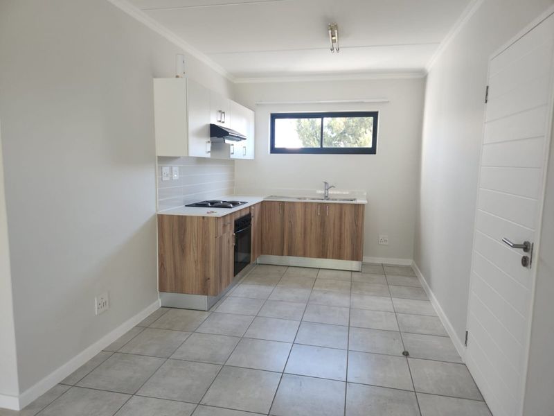 A clean, modern kitchen featuring wood-finish lower cabinetry, white upper cabinets, a built-in oven and hob, and neutral tiled flooring.