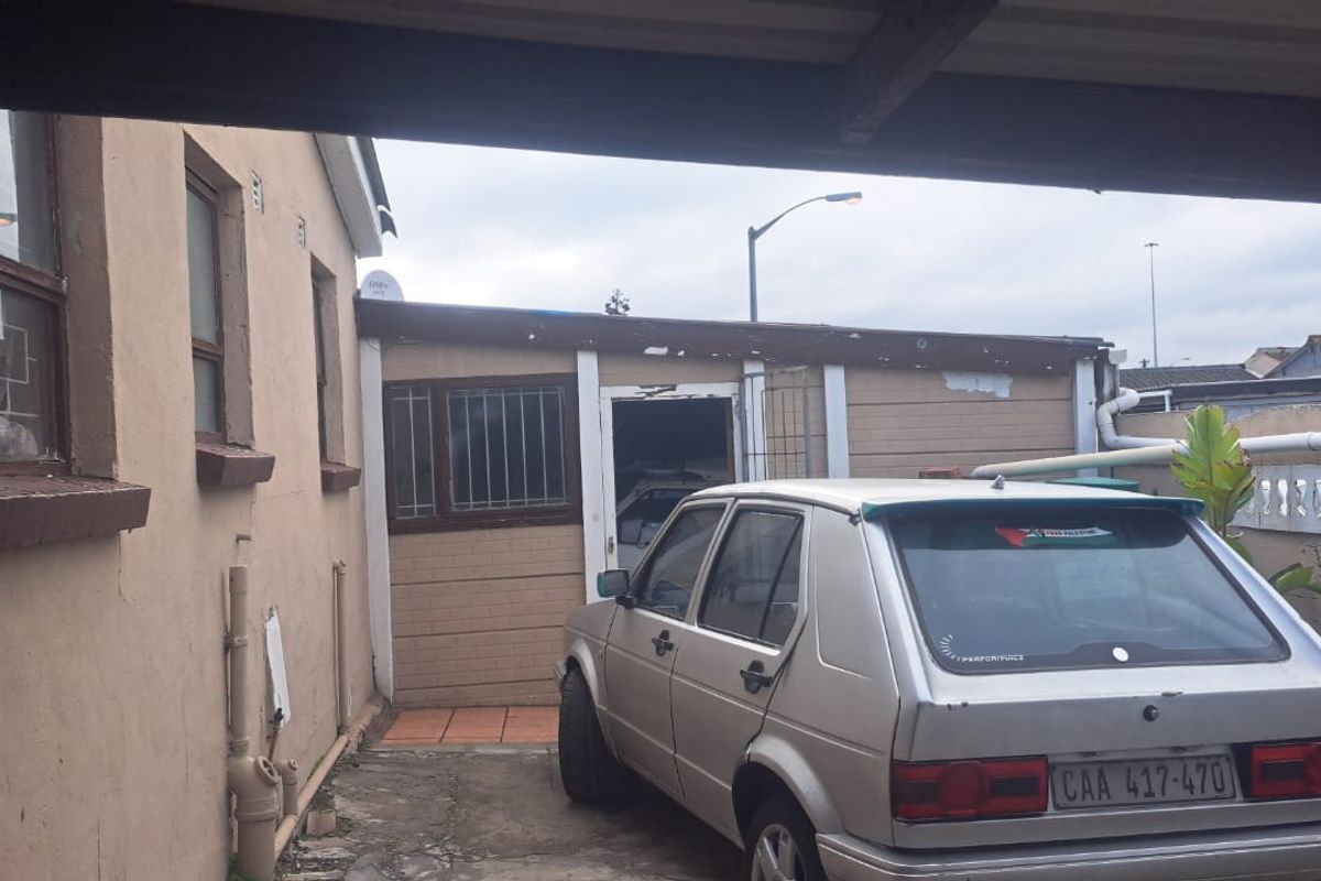 Rear exterior view of the property showing a paved area, boundary wall, and building facade with visible signs of weathering and paint deterioration.