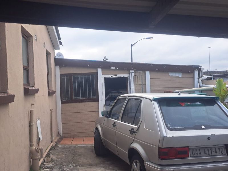 Rear exterior view of the property showing a paved area, boundary wall, and building facade with visible signs of weathering and paint deterioration.
