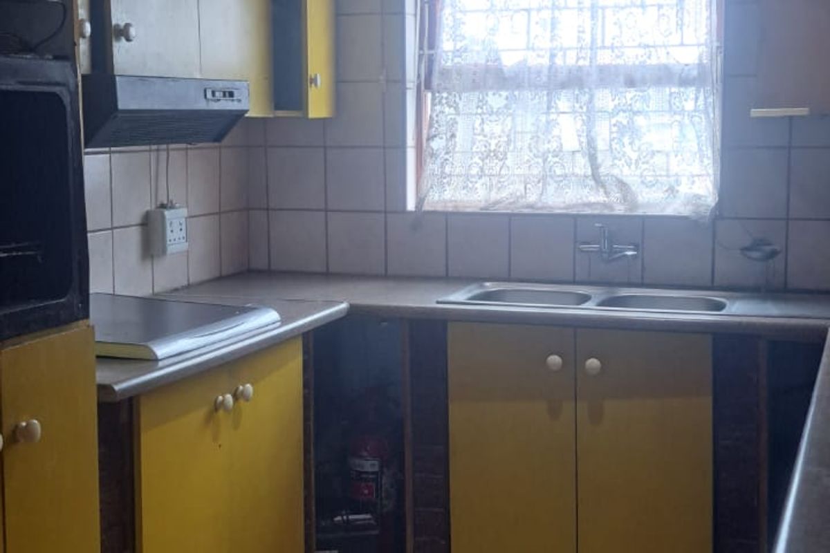 A dated kitchen featuring yellow cabinetry, tiled flooring, a double sink, and built-in extractor fan, offering significant potential for modernization and renovation.