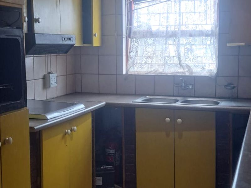 A dated kitchen featuring yellow cabinetry, tiled flooring, a double sink, and built-in extractor fan, offering significant potential for modernization and renovation.