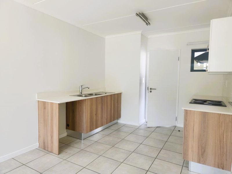 A clean, modern kitchen featuring light wood-finish cabinetry, white countertops, a stainless steel sink, and a built-in ceramic hob on tiled flooring.