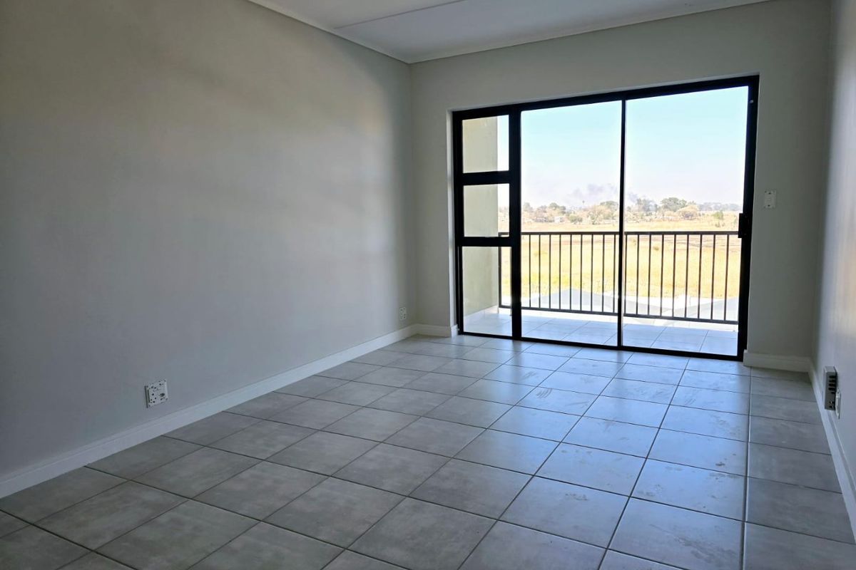 An empty, well-lit living area featuring neutral tiled flooring and a large sliding glass door providing access to a private balcony.