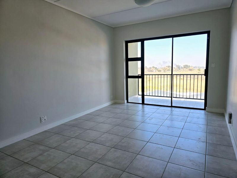 An empty, well-lit living area featuring neutral tiled flooring and a large sliding glass door providing access to a private balcony.