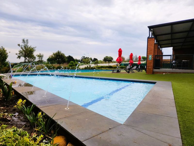 A well-maintained outdoor pool area featuring water fountains, stone coping, and an adjacent covered patio with brick structural elements.