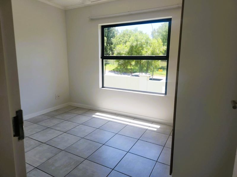 A bright, empty bedroom featuring neutral tiled flooring and a large window providing natural light and exterior views.