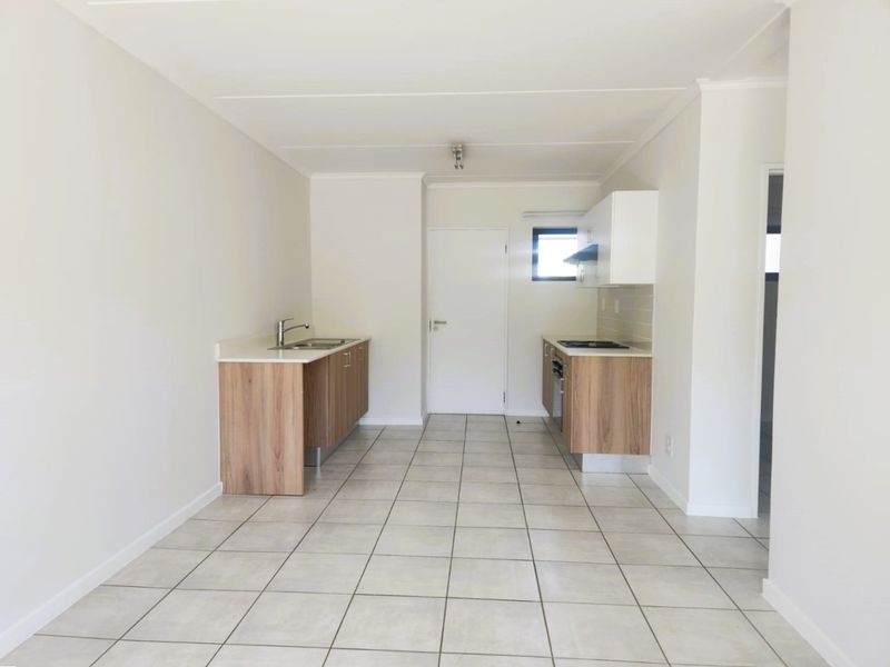A clean, modern, and empty kitchen featuring light wood-finish cabinetry, tiled flooring, and integrated appliances including a hob, oven, and extractor fan.