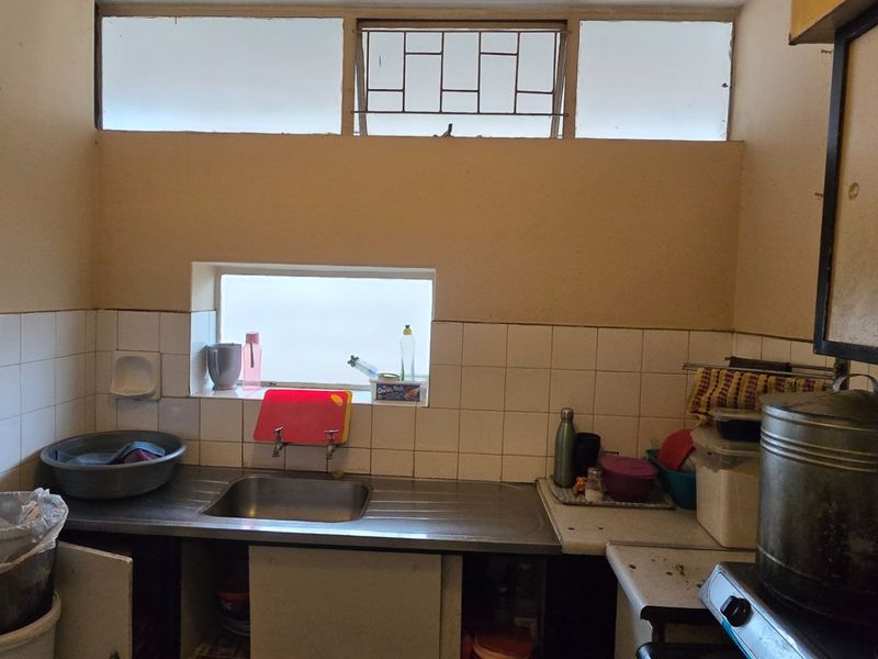 A functional kitchen area featuring a stainless steel sink, tiled splashback, and high-level windows providing natural light.
