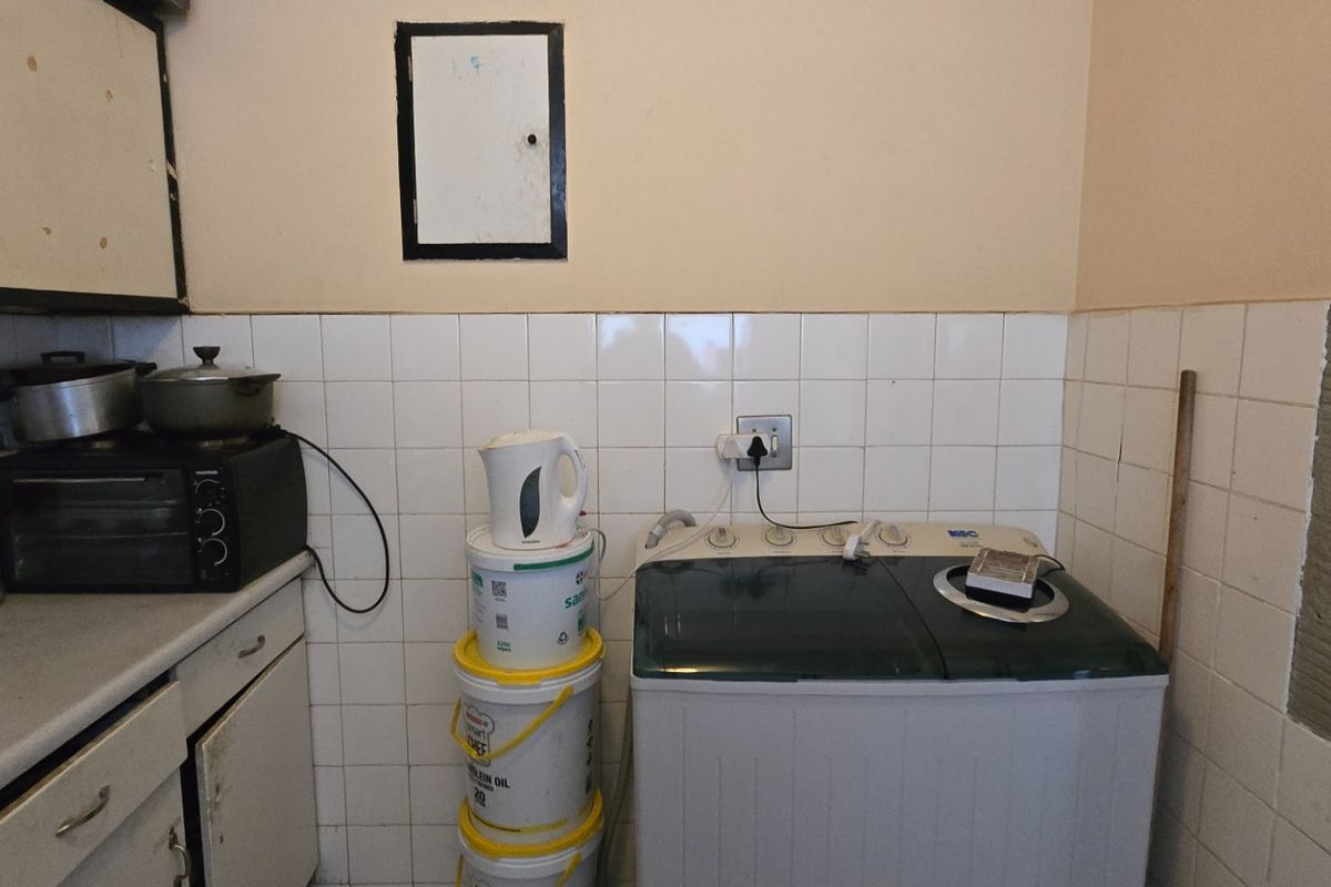 A functional laundry area featuring tiled splashbacks and built-in cabinetry, currently showing signs of wear and incomplete wall tiling.