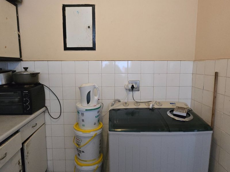 A functional laundry area featuring tiled splashbacks and built-in cabinetry, currently showing signs of wear and incomplete wall tiling.