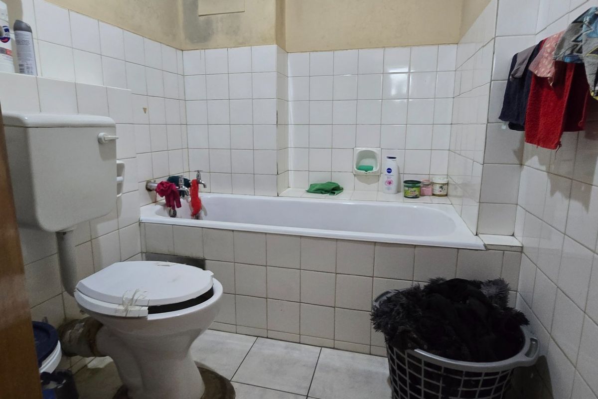A dated bathroom featuring a standard bathtub, toilet, and full-height ceramic wall tiling. The space requires cosmetic updates and maintenance.