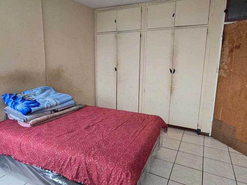 A bedroom featuring built-in cupboards and tiled flooring, currently requiring cosmetic updates and wall repairs to improve its overall condition.