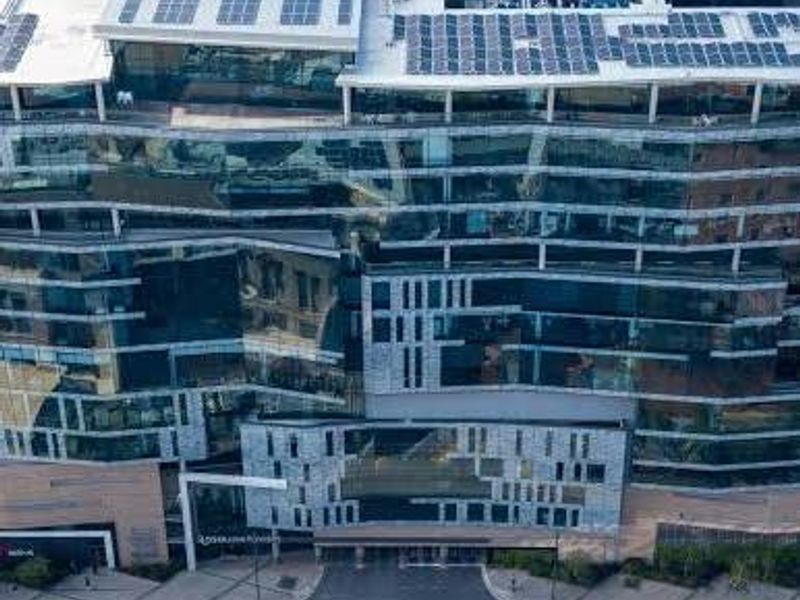Aerial view of a modern multi-story commercial office building featuring a glass facade and extensive rooftop solar panel installation.