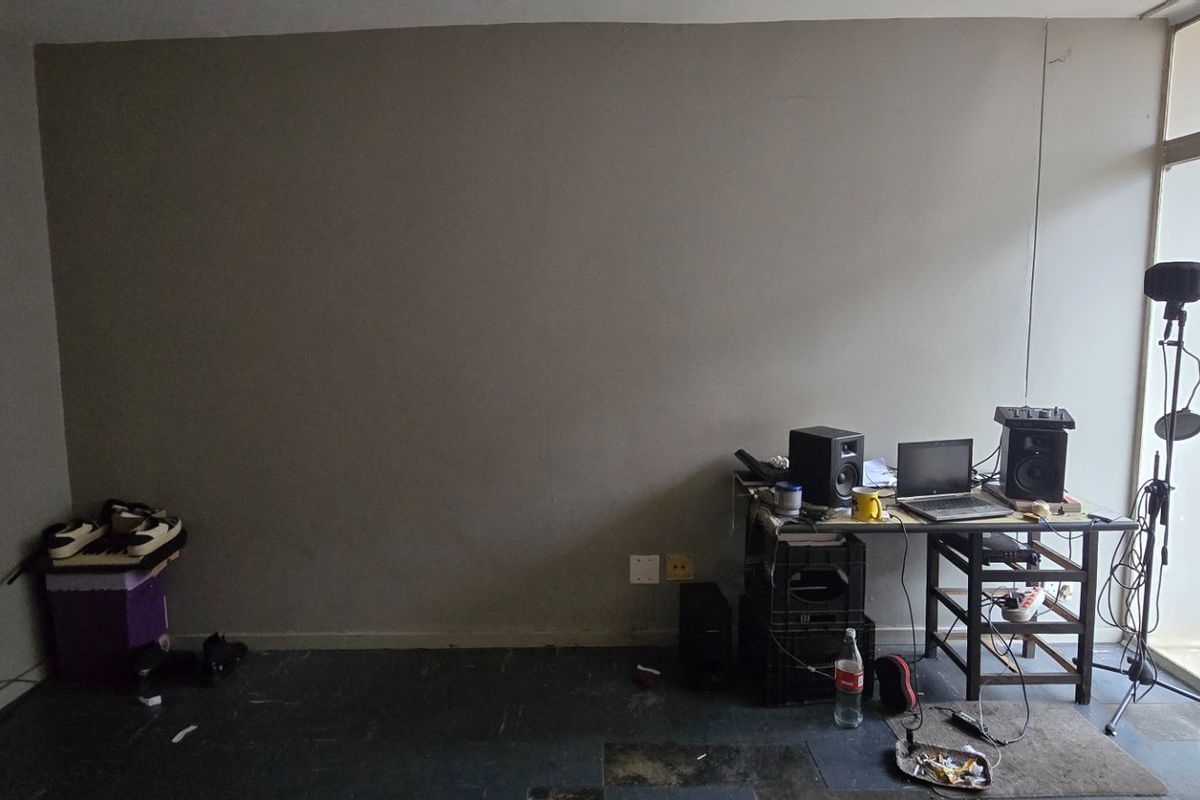 A living area featuring a large blank wall, dark flooring, and access to a balcony through a sliding glass door.