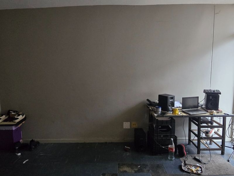 A living area featuring a large blank wall, dark flooring, and access to a balcony through a sliding glass door.
