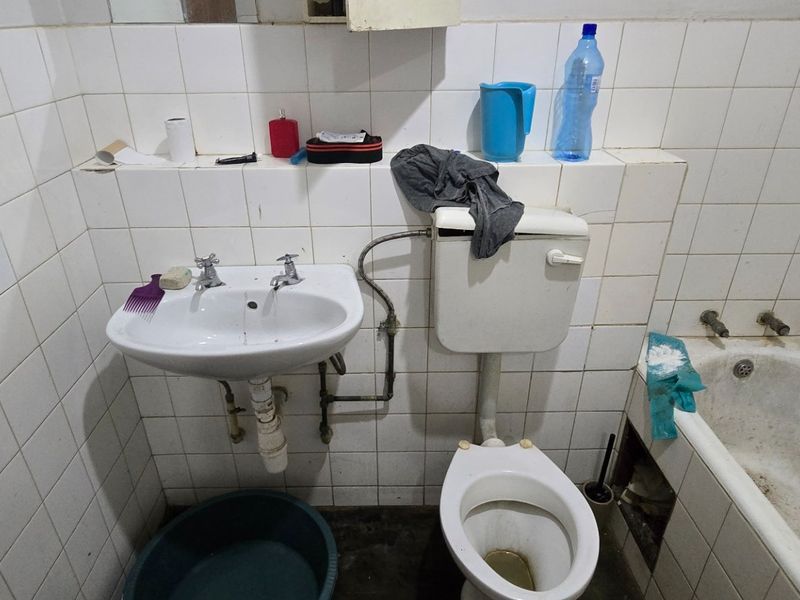 A dated bathroom featuring a wall-mounted basin, flush toilet, and built-in bathtub with tiled wall finishes, requiring renovation and modernization.
