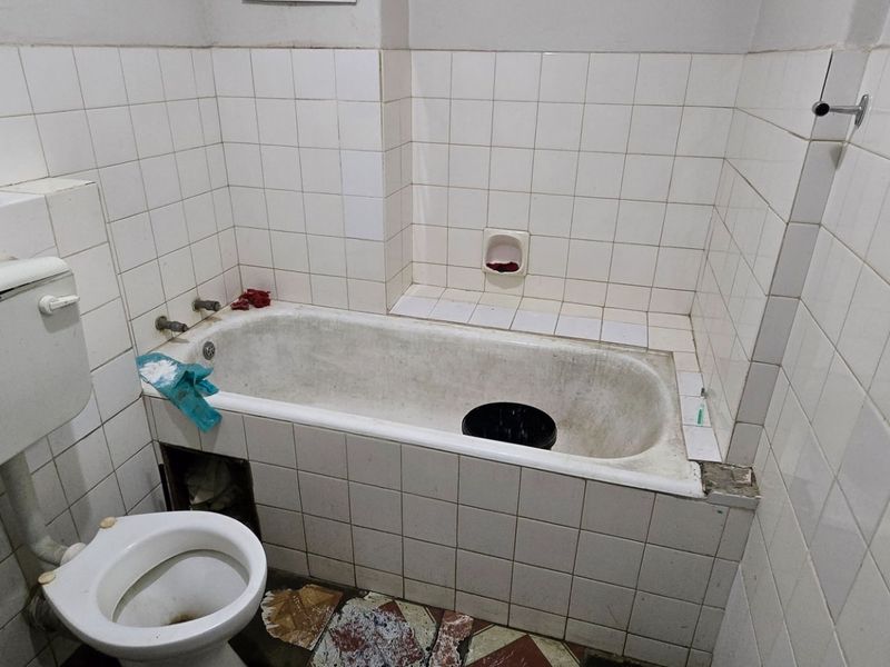 A dated bathroom featuring a standard bathtub, toilet, and white ceramic wall tiles, requiring significant renovation and cosmetic updates to improve its condition.