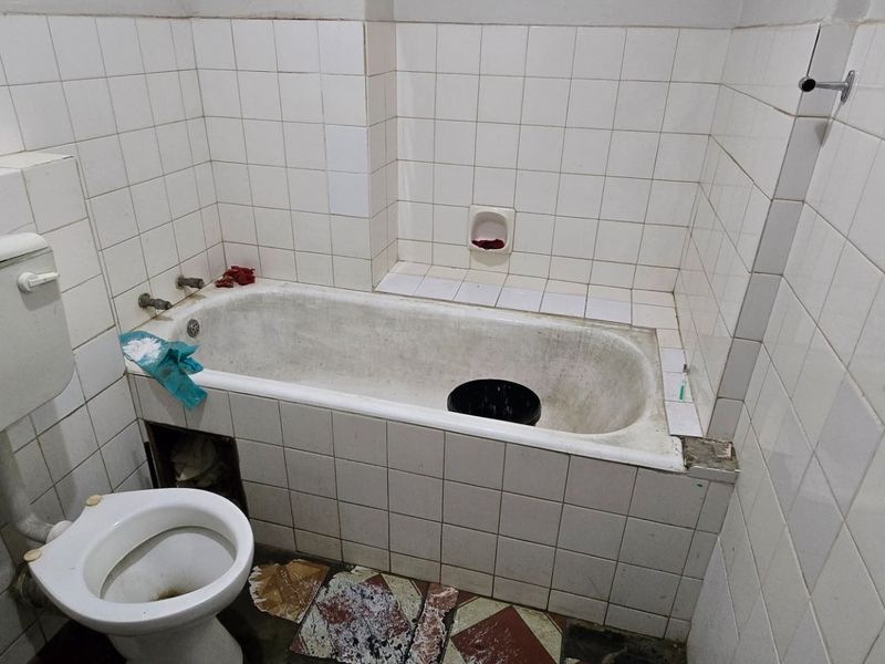 A dated bathroom featuring a bathtub, toilet, and washbasin with white wall tiling. The space requires renovation and repair of finishes.
