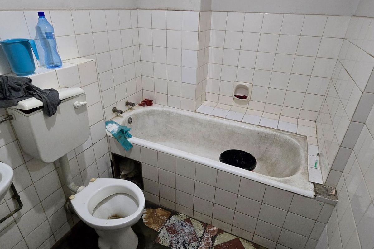 A dated bathroom featuring a standard bathtub, toilet, and washbasin with white wall tiling, requiring significant renovation and modernization of fixtures and finishes.