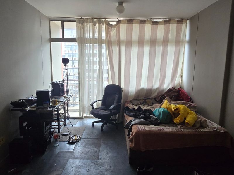 A bedroom featuring a sliding glass door with balcony access and basic ceiling lighting, requiring cosmetic updates to improve the overall finish.