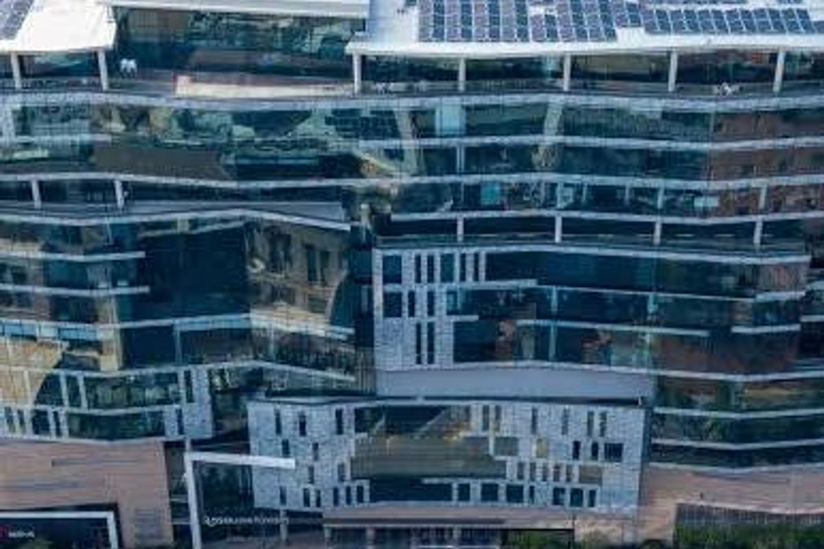 Aerial view of a modern multi-story commercial office building featuring a glass facade and extensive rooftop solar panel installation.
