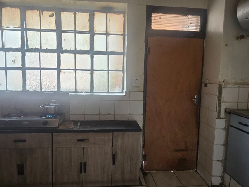 A functional kitchen featuring built-in cabinetry, a gas stove, tiled splashbacks, and a steel-framed window, offering a practical layout for renovation.