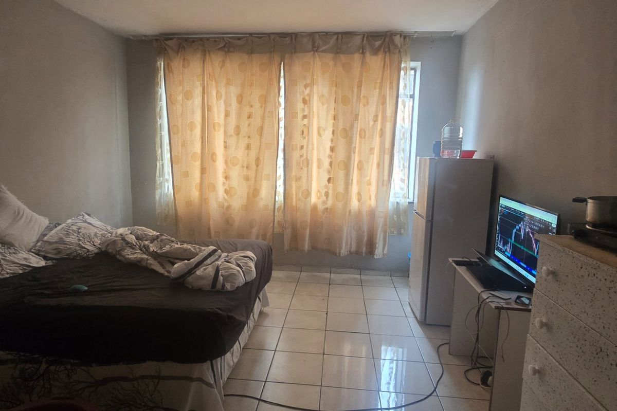 A bedroom featuring tiled flooring and natural light through window curtains, requiring cosmetic updates to the wall finishes.