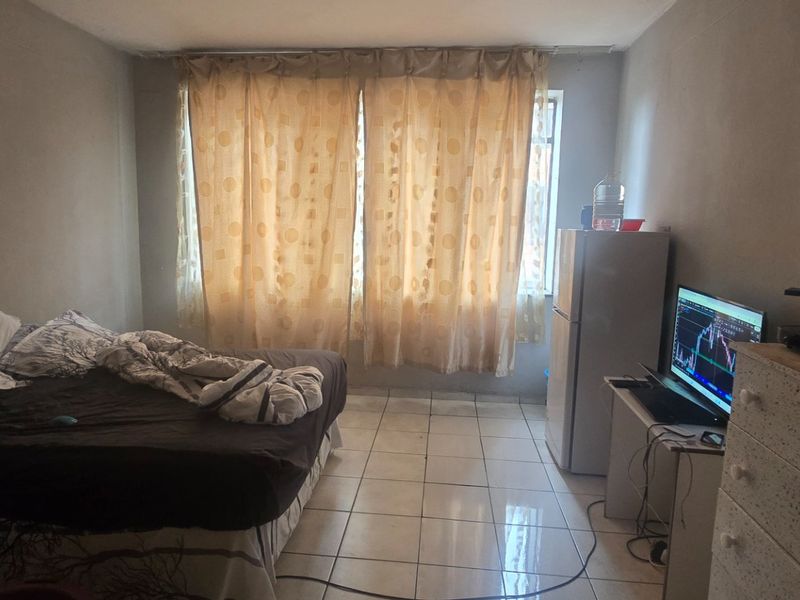 A bedroom featuring tiled flooring and natural light through window curtains, requiring cosmetic updates to the wall finishes.