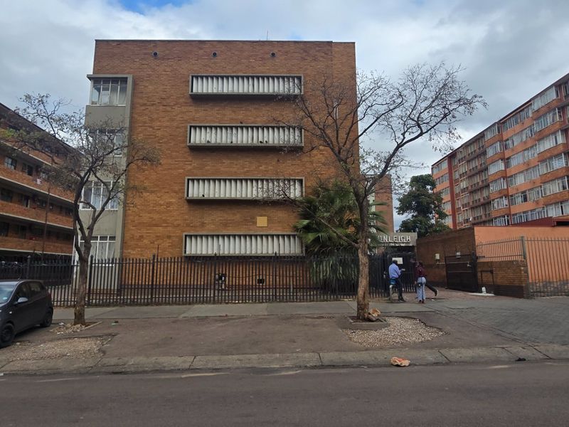 Street view of a multi-story brick apartment building featuring metal security fencing, gated entrance, and louvre window shutters.