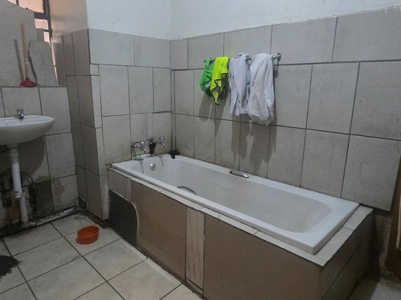A dated bathroom featuring a bathtub and pedestal basin with tiled walls and flooring, requiring significant renovation and repair to fixed finishes.