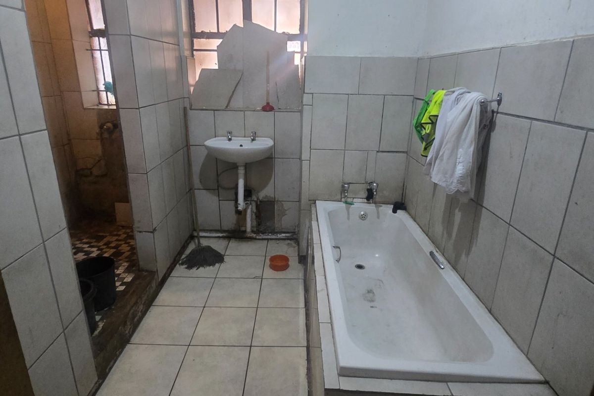 A dated bathroom featuring a bathtub and pedestal basin, requiring significant renovation and repair to the wall tiling and overall finishes.