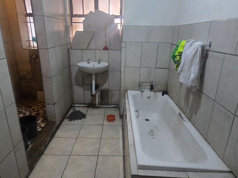 A dated bathroom featuring a bathtub and pedestal basin, requiring significant renovation and repair to the wall tiling and overall finishes.