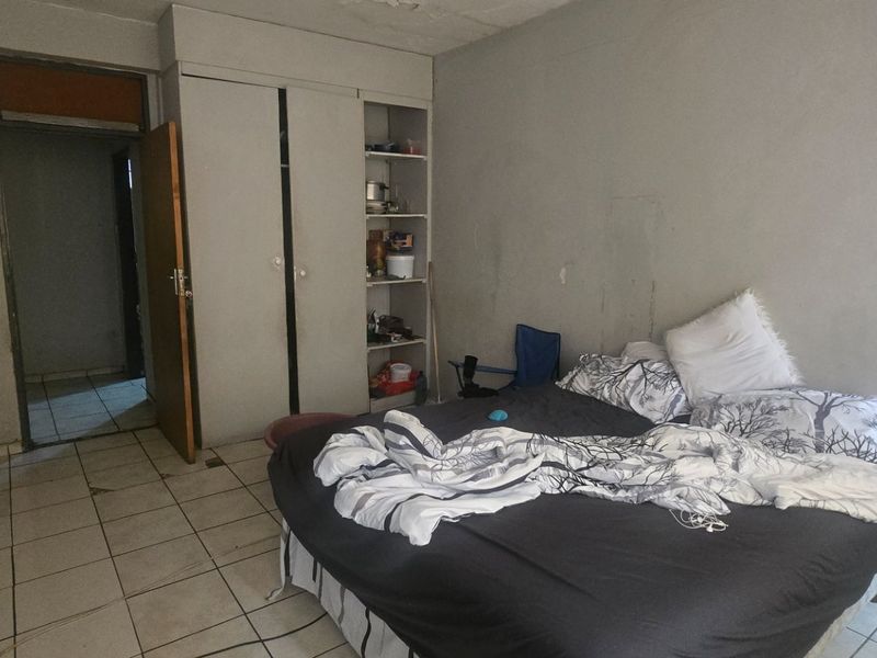 Bedroom featuring tiled flooring and a built-in wardrobe with open shelving, requiring cosmetic updates to the wall finishes.