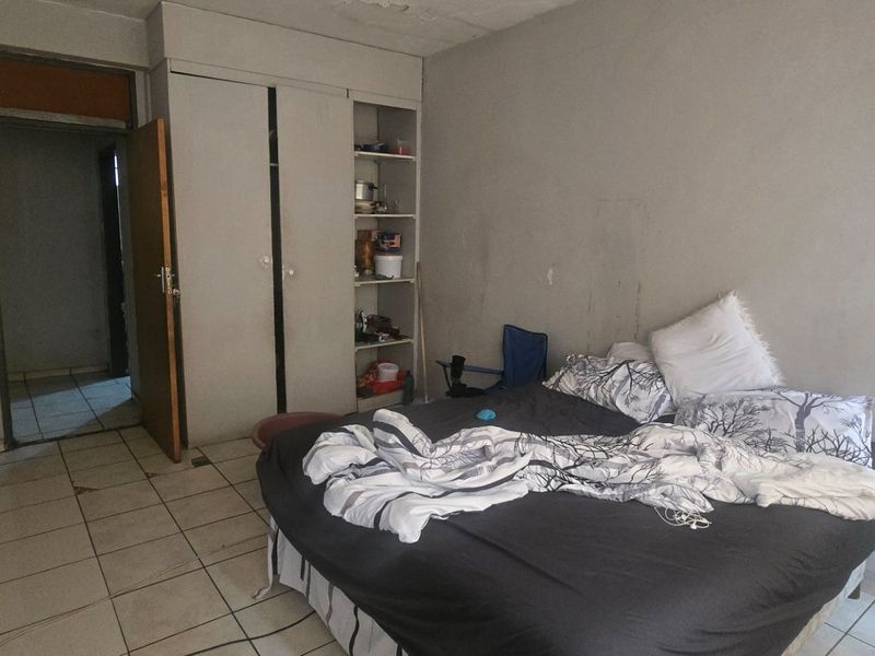 A bedroom featuring built-in wardrobe storage and tiled flooring, currently requiring maintenance and cosmetic updates to the walls and ceiling.