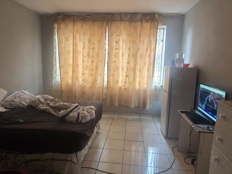 A bedroom featuring tiled flooring and window curtain rails, currently used as a multi-functional living space.