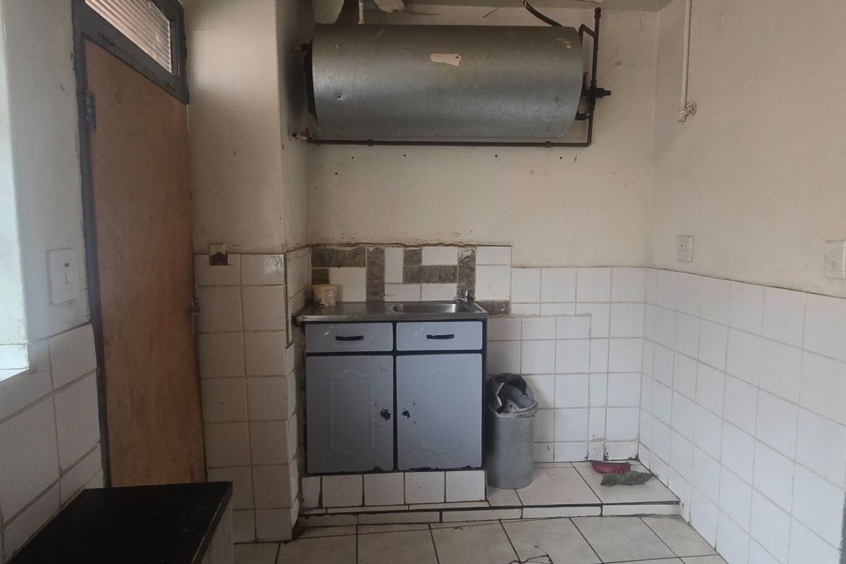 A small, dated kitchen area featuring basic cabinetry, a sink, and a wall-mounted geyser, requiring significant renovation and cosmetic updates.