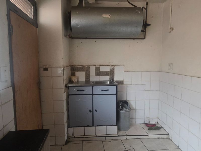 A small, dated kitchen area featuring basic cabinetry, a sink, and a wall-mounted geyser, requiring significant renovation and cosmetic updates.