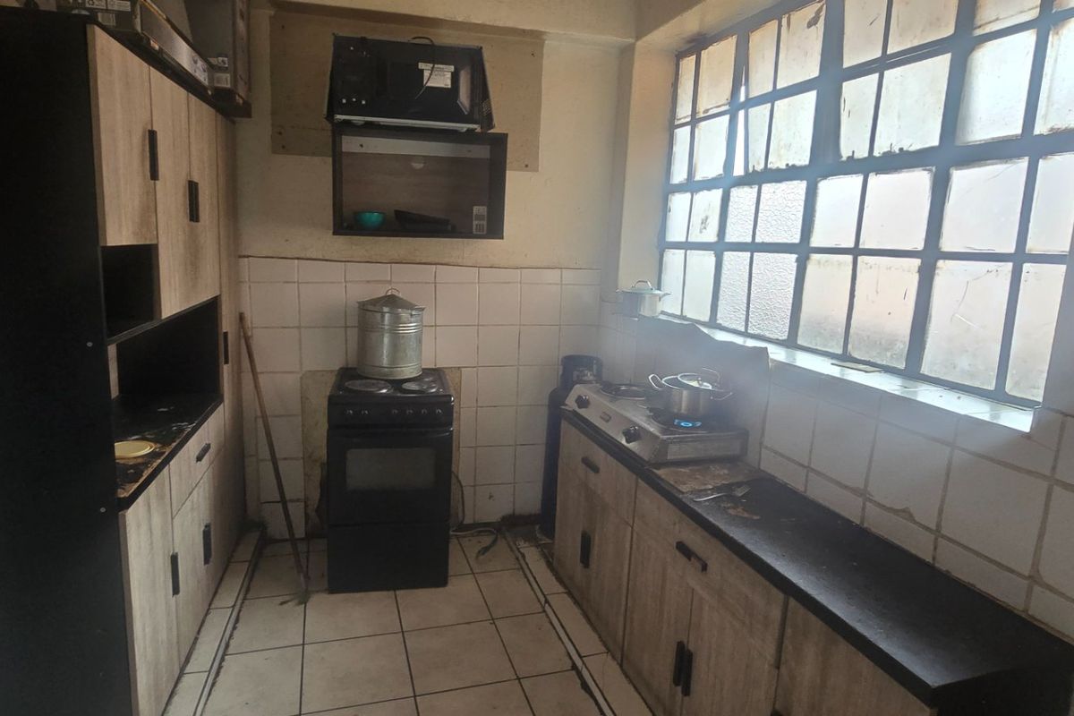 A dated kitchen featuring built-in cabinetry, tiled backsplash, and tiled flooring, requiring cosmetic updates to modernize the space.