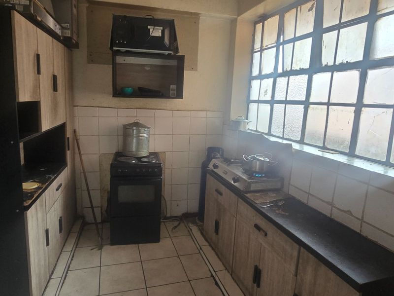 A dated kitchen featuring built-in cabinetry, tiled backsplash, and tiled flooring, requiring cosmetic updates to modernize the space.