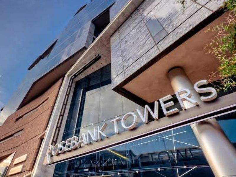 Low-angle exterior view of the modern glass and metal facade of Rosebank Towers, showcasing contemporary architectural design and prominent building signage.