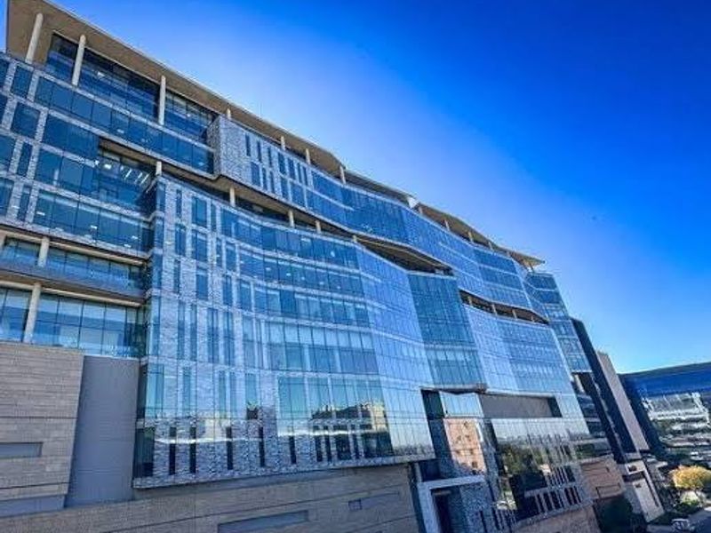 A modern multi-story commercial office building featuring an extensive glass curtain wall facade and stone cladding elements.