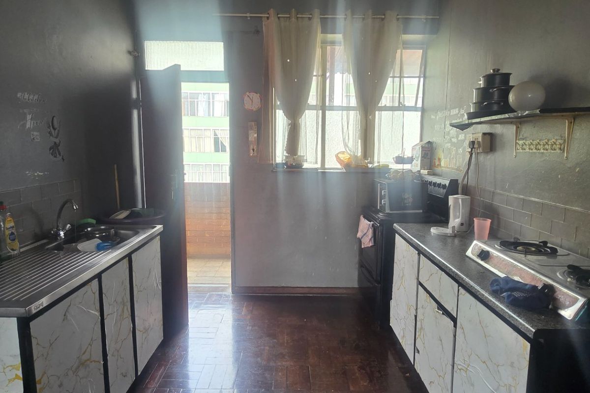 A functional kitchen featuring built-in cabinetry, a gas hob, stainless steel sink, and parquet flooring, offering potential for modernization and aesthetic updates.