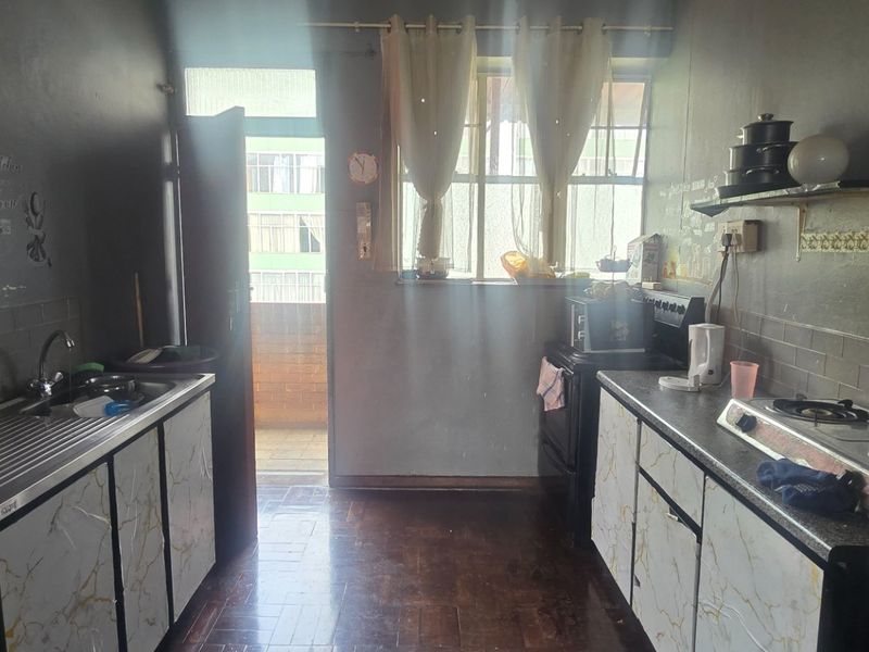 A functional kitchen featuring built-in cabinetry, a gas hob, stainless steel sink, and parquet flooring, offering potential for modernization and aesthetic updates.