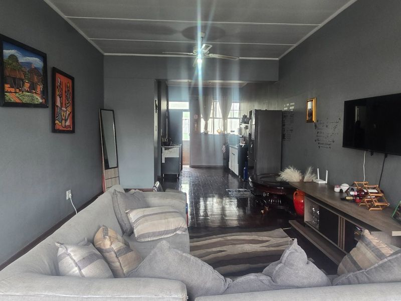 Open plan living area featuring dark wood flooring and a ceiling fan, flowing into a kitchen space at the rear.