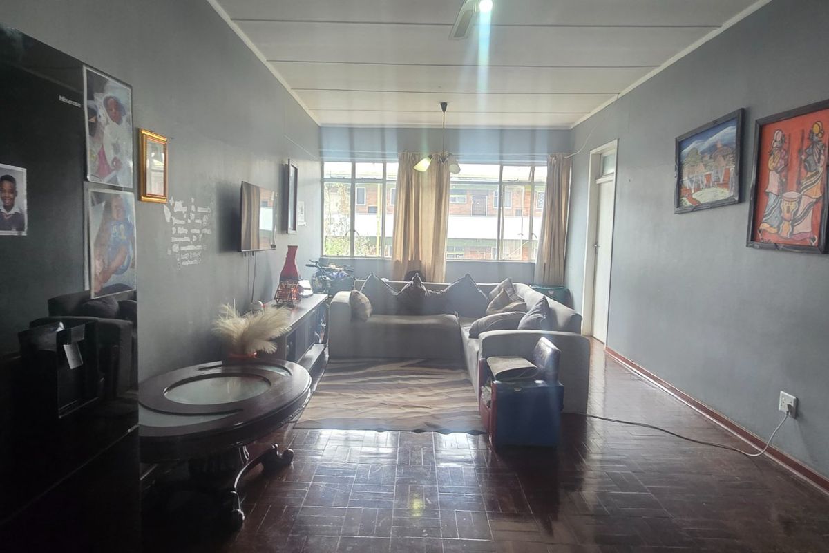 A spacious living area featuring dark parquet flooring, a ceiling fan, and large windows that provide natural light.