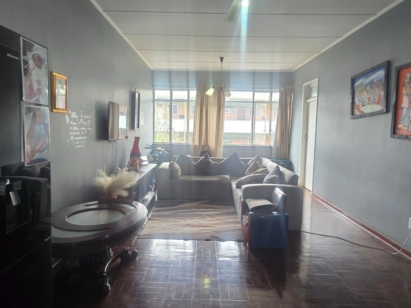 A spacious living area featuring dark parquet flooring, a ceiling fan, and large windows that provide natural light.