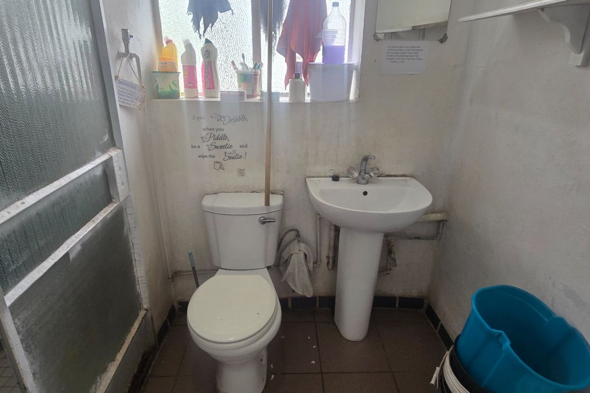 A compact bathroom featuring a pedestal basin, toilet, and shower enclosure. The space requires cosmetic updates and maintenance to improve its overall condition.