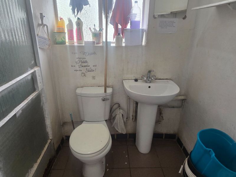 A compact bathroom featuring a pedestal basin, toilet, and shower enclosure. The space requires cosmetic updates and maintenance to improve its overall condition.